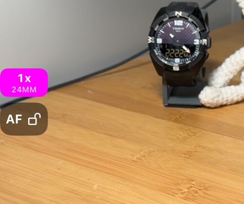 El borde izquierdo del visor: el botón AF con el candado abierto y encima la plaquita de zoom con 1x y 24MM