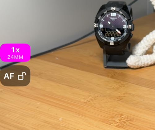 El borde izquierdo del visor: el botón AF con el candado abierto y encima la plaquita de zoom con 1x y 24MM